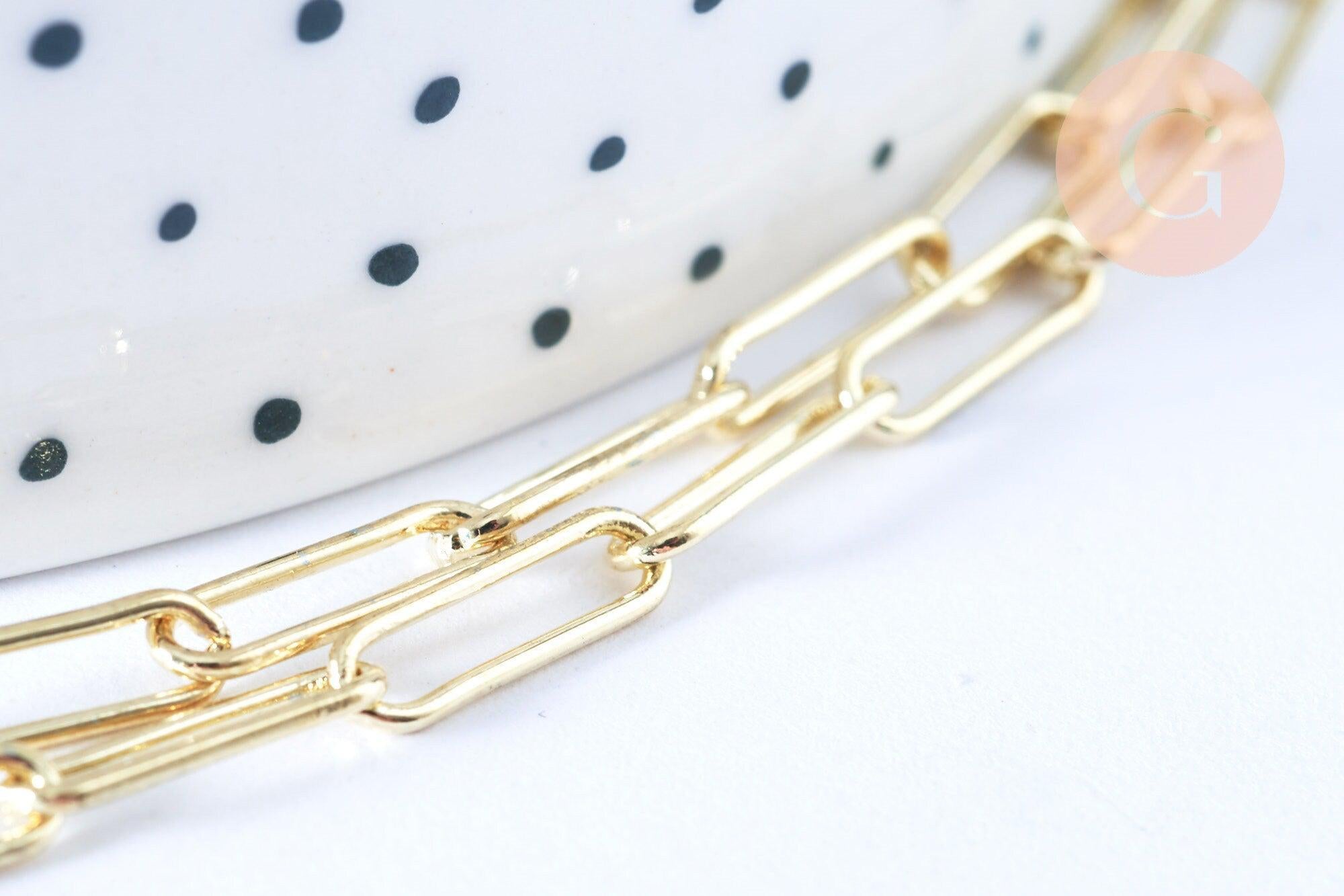 Close-up of Collier Chaine laiton doré clair maille rectangle, featuring a shiny gold chain on a white surface with a polka-dotted ceramic object in the background.