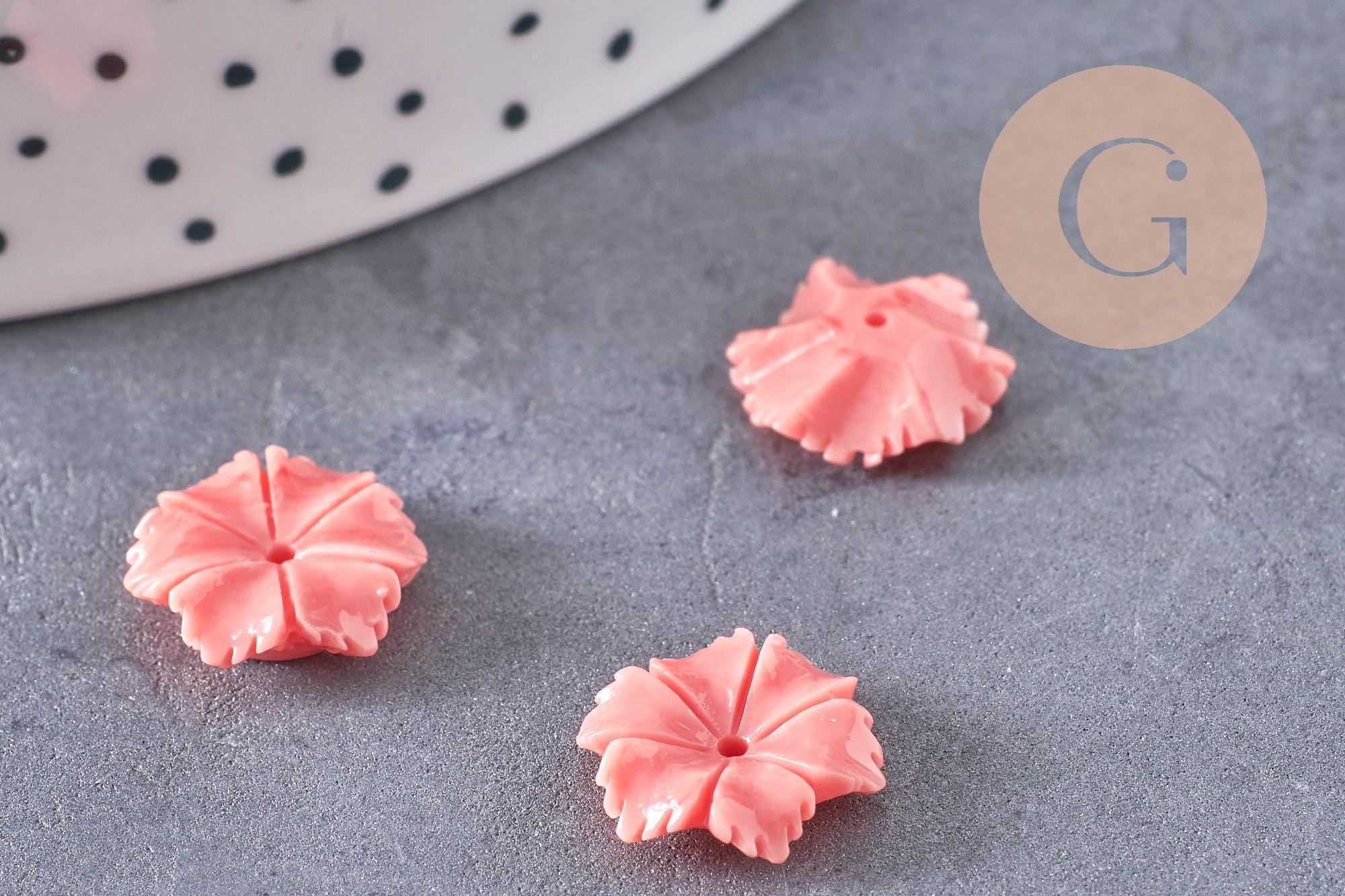 Close-up of EP-Perle fleur résine rose, soft pink flower-shaped resin beads for jewelry making, on a gray stone surface, partially visible white ceramic plate edge.