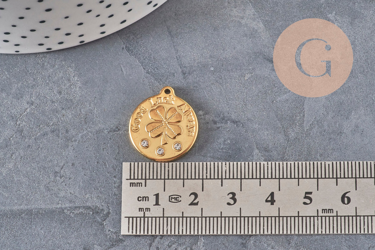 Pendentif médaille trèfle 20mm en acier doré avec zircons et inscription Good Luck Always sur fond gris.