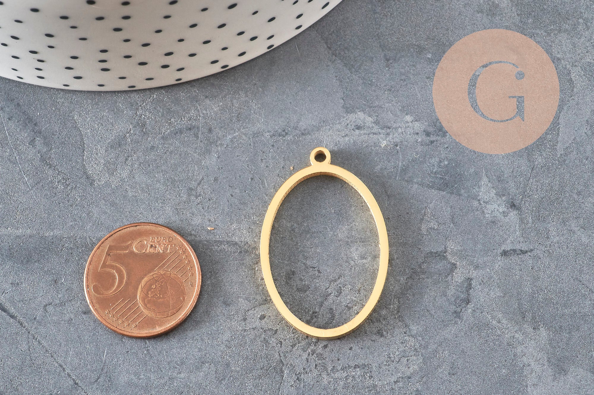 Pendentif ovale doré IP en acier inoxydable 304 sans fond de 35mm, à côté d'une pièce de 5 centimes.