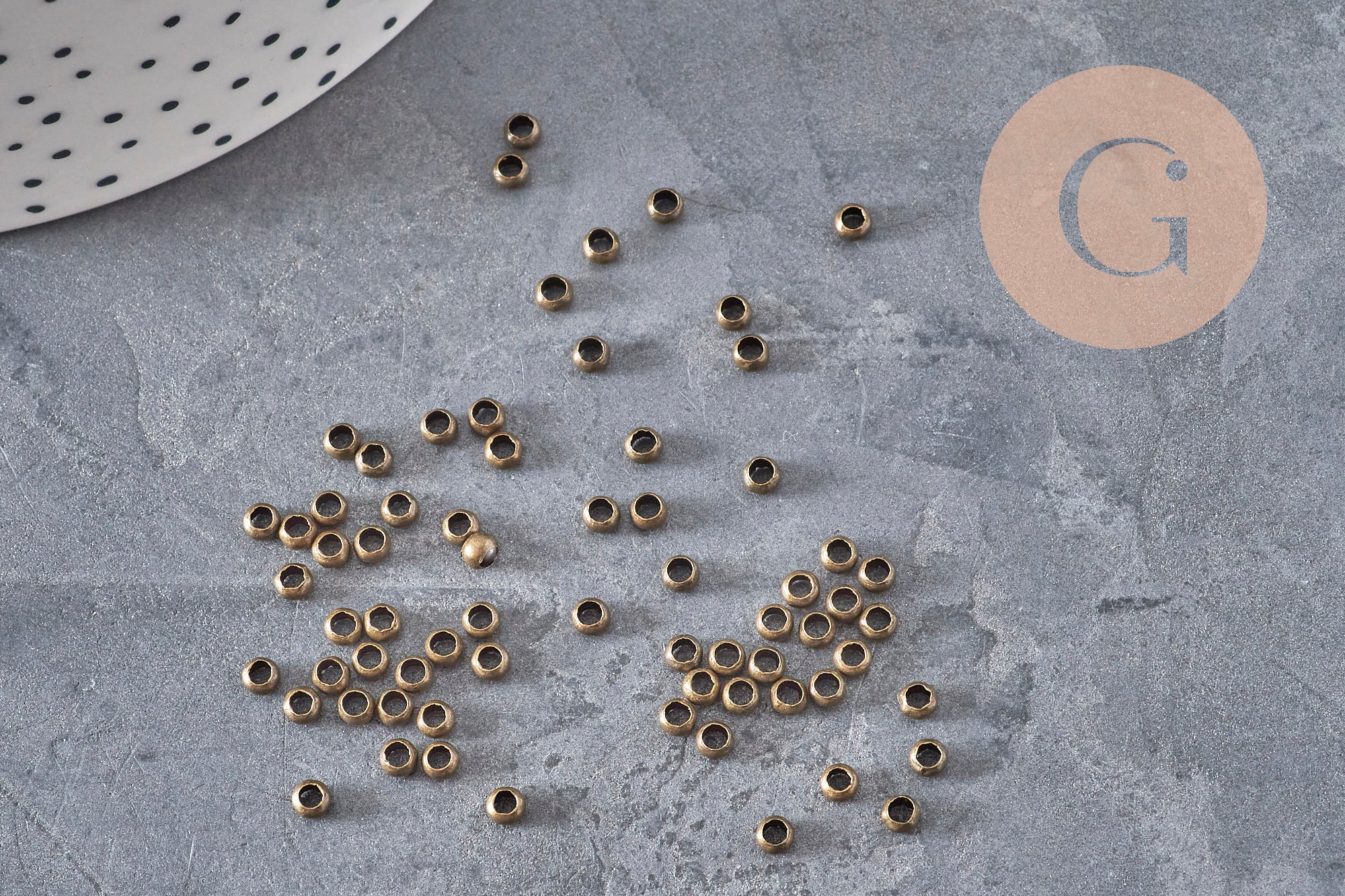 Petites perles à écraser rondelles en laiton couleur bronze, 3x2mm, sur fond gris texturé.