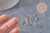 Petites perles à écraser en laiton or rose 2x1.2mm, tenues sur un doigt et éparpillées sur une surface grise.