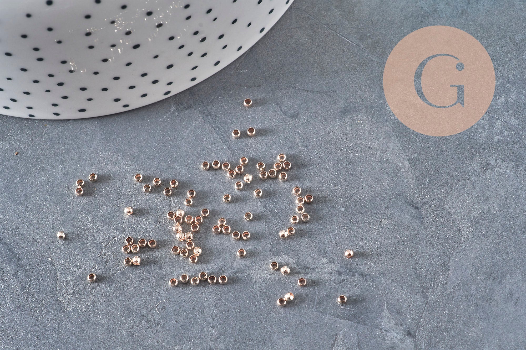 Perles à écraser en laiton or rose 2x1.2mm, dispersées sur une surface grise.