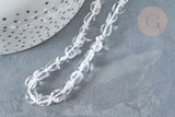 Translucent pebble-shaped glass beads, Perles cristal de roche roulée pierre brute, lie on a dark gray stone surface, beside a dotted white ceramic pot.